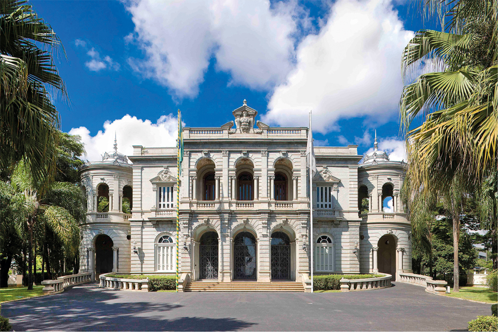 Fachada do Palácio da Liberdade, com sua arquitetura histórica e imponente, cercada por palmeiras e céu azul ao fundo.