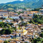 Vista panorâmica de Ouro Preto, em Minas Gerais, destacando a arquitetura colonial com igrejas históricas, casas com telhados de barro e montanhas verdes ao fundo.