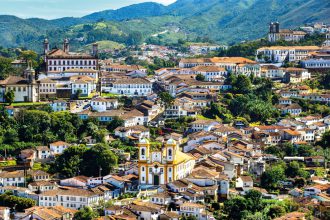 Vista panorâmica de Ouro Preto, em Minas Gerais, destacando a arquitetura colonial com igrejas históricas, casas com telhados de barro e montanhas verdes ao fundo.